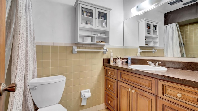 full bathroom with a wainscoted wall, tile walls, toilet, and vanity