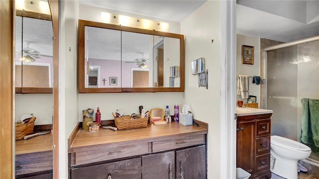 bathroom with toilet, ceiling fan, vanity, and a shower stall