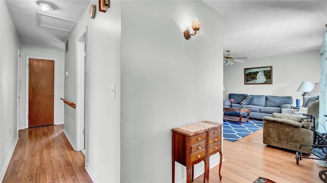 hall featuring attic access, baseboards, and light wood-style flooring