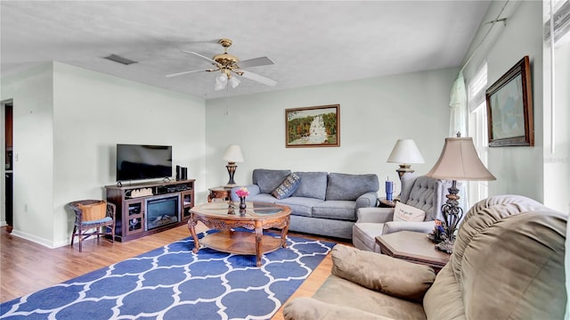 living area featuring a ceiling fan, visible vents, baseboards, and wood finished floors