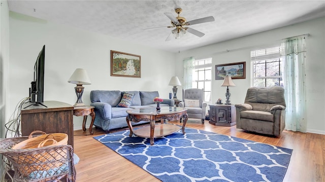 living area featuring a textured ceiling, wood finished floors, a ceiling fan, and baseboards