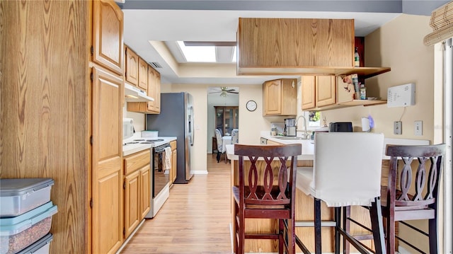 kitchen featuring white range with electric stovetop, light countertops, a sink, under cabinet range hood, and a kitchen breakfast bar