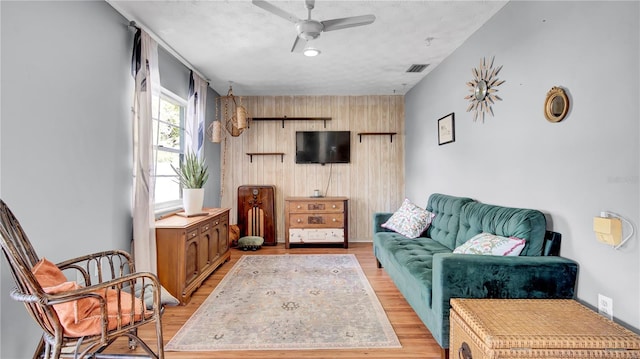 living room with light wood-style floors, visible vents, ceiling fan, and wood walls