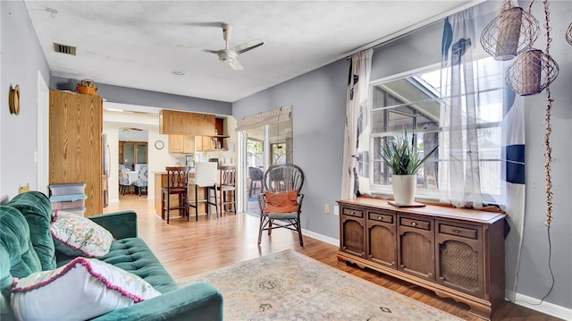 living room featuring visible vents, ceiling fan, baseboards, and wood finished floors