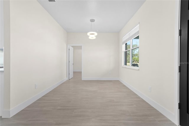 unfurnished room with light wood-type flooring, visible vents, and baseboards