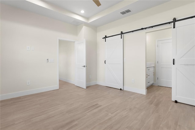 unfurnished bedroom featuring a barn door, light wood-type flooring, and visible vents