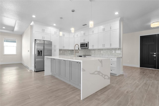 kitchen featuring a large island, backsplash, appliances with stainless steel finishes, white cabinets, and light wood-type flooring