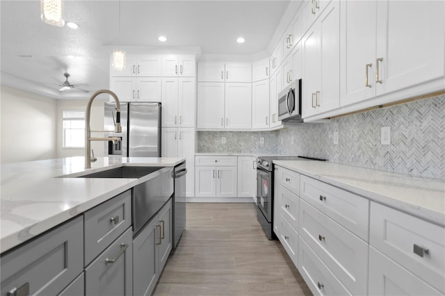 kitchen with white cabinets, appliances with stainless steel finishes, backsplash, gray cabinets, and a sink