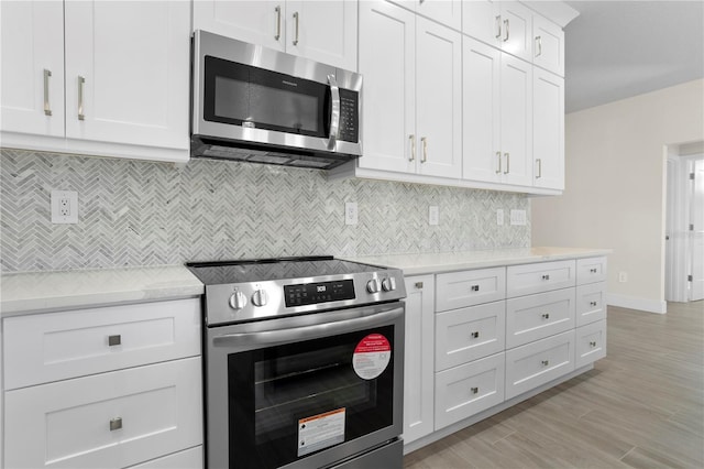 kitchen with white cabinets, light countertops, appliances with stainless steel finishes, light wood-type flooring, and backsplash