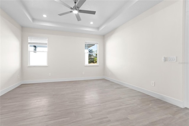 unfurnished room with a tray ceiling, light wood finished floors, recessed lighting, a ceiling fan, and baseboards