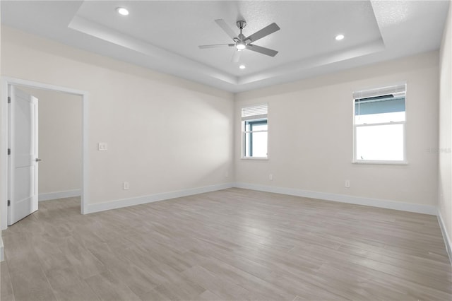 empty room with a tray ceiling, light wood-type flooring, recessed lighting, and baseboards