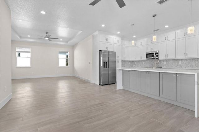 kitchen with a tray ceiling, stainless steel appliances, light countertops, decorative backsplash, and white cabinetry