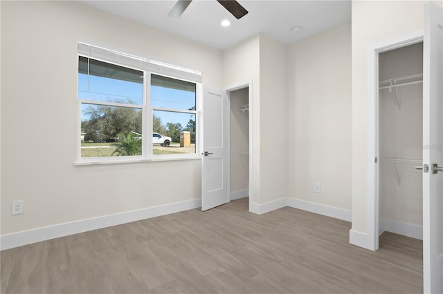 unfurnished bedroom featuring recessed lighting, wood finished floors, two closets, and baseboards