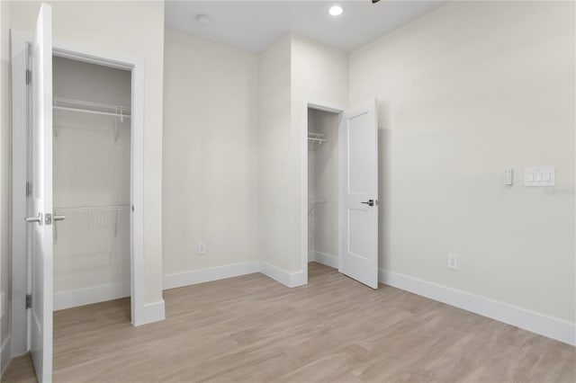 unfurnished bedroom with baseboards, light wood finished floors, recessed lighting, and multiple closets