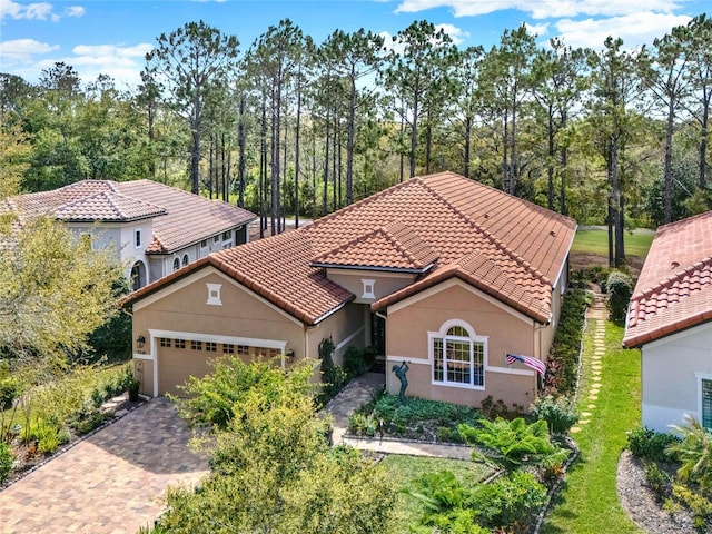 mediterranean / spanish home featuring a garage, decorative driveway, a tiled roof, and stucco siding