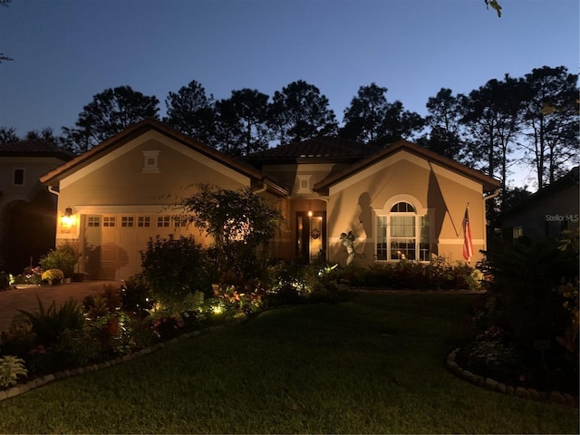 mediterranean / spanish home featuring a garage, driveway, a front lawn, and stucco siding