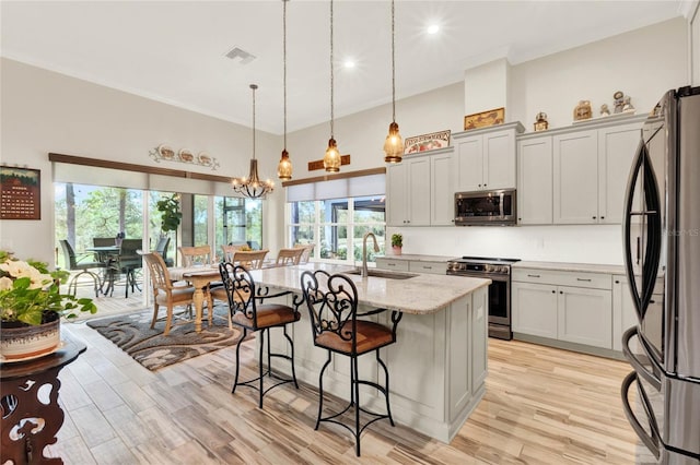 kitchen with light wood finished floors, light stone counters, appliances with stainless steel finishes, a breakfast bar, and a sink