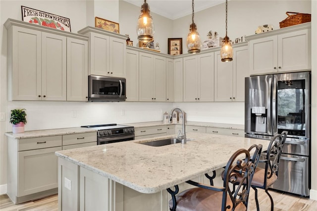 kitchen with light stone counters, a breakfast bar area, a sink, appliances with stainless steel finishes, and decorative light fixtures