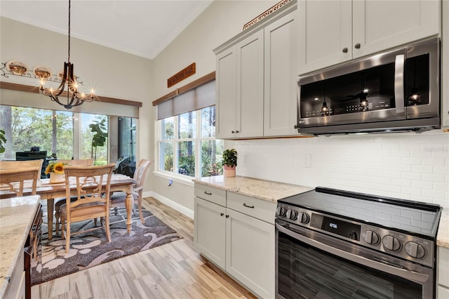 kitchen featuring light wood finished floors, backsplash, light stone countertops, stainless steel appliances, and a notable chandelier