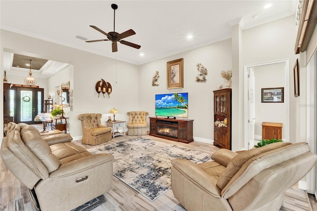 living room featuring ornamental molding, a glass covered fireplace, a ceiling fan, light wood-type flooring, and baseboards