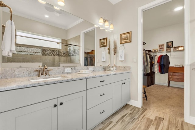 bathroom featuring double vanity, a stall shower, ornamental molding, a walk in closet, and a sink