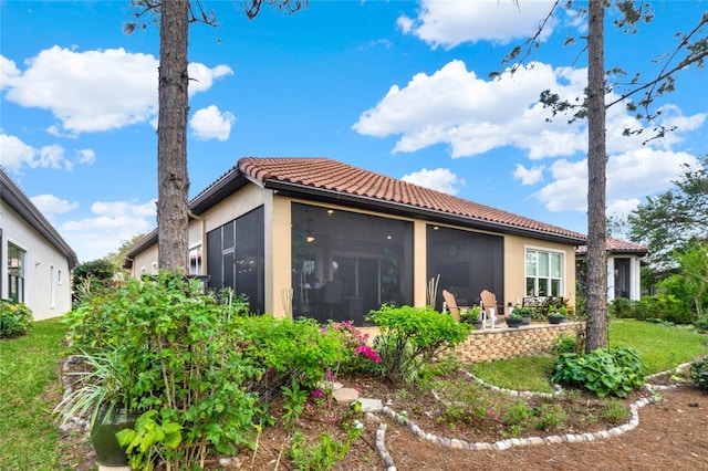 back of house featuring a tile roof, stucco siding, a lawn, a sunroom, and a patio area