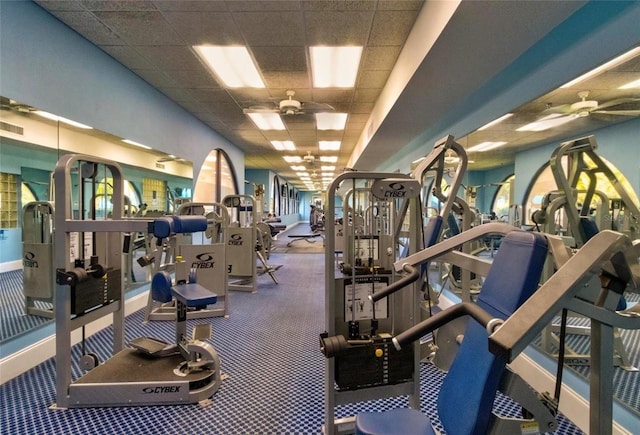 exercise room with a paneled ceiling, ceiling fan, and baseboards