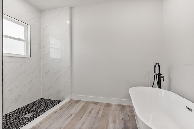 bathroom with wood finished floors, walk in shower, a freestanding tub, and baseboards