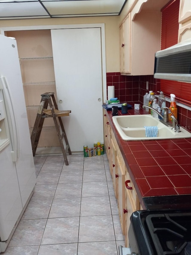 kitchen featuring tile countertops, light tile patterned floors, decorative backsplash, a sink, and white fridge with ice dispenser