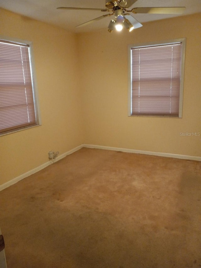 carpeted empty room featuring a ceiling fan and baseboards