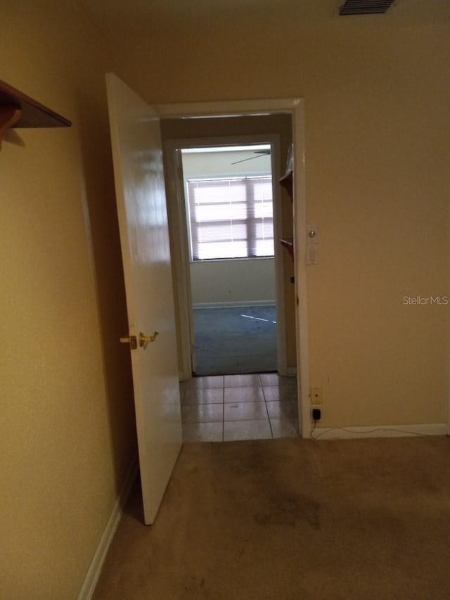 hallway featuring carpet floors, tile patterned flooring, visible vents, and baseboards