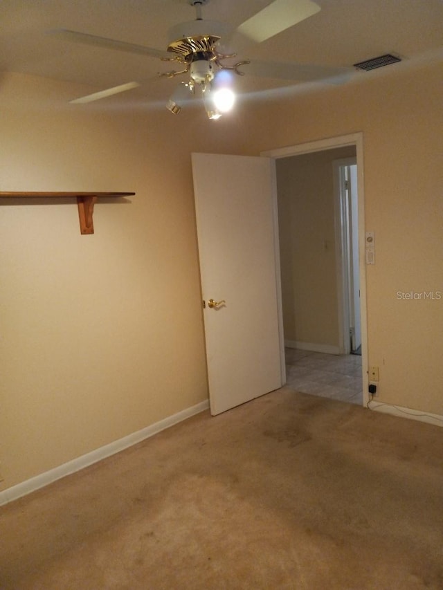 spare room with a ceiling fan, light colored carpet, visible vents, and baseboards