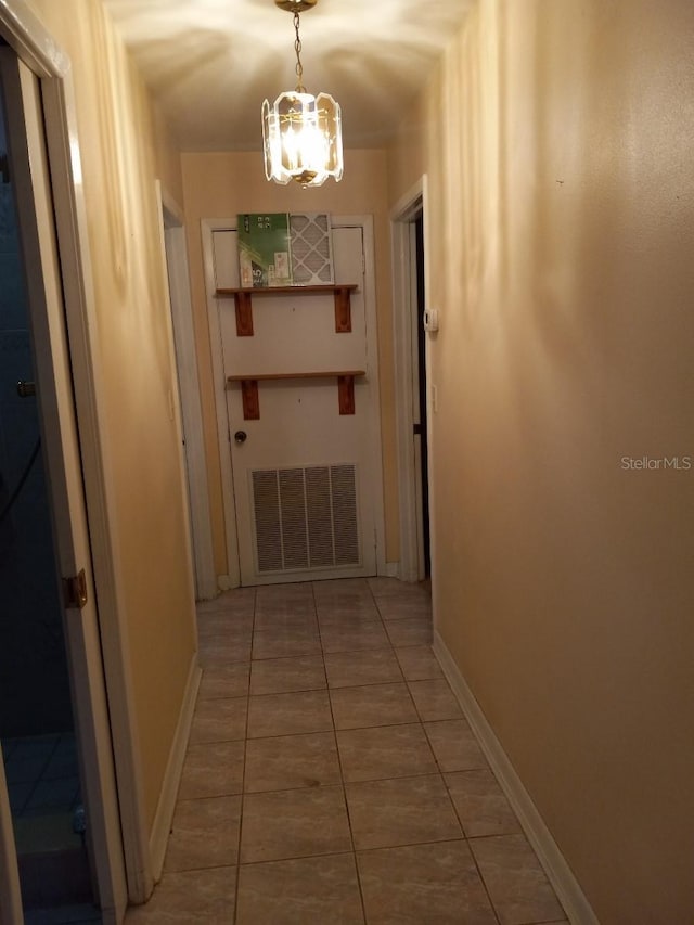 corridor featuring baseboards, light tile patterned floors, visible vents, and a notable chandelier