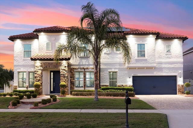 mediterranean / spanish-style house with decorative driveway, stucco siding, an attached garage, stone siding, and a front lawn