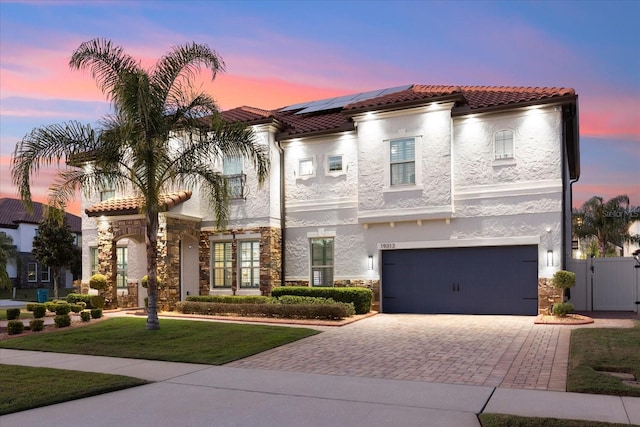 mediterranean / spanish house with stone siding, a tile roof, a gate, roof mounted solar panels, and stucco siding