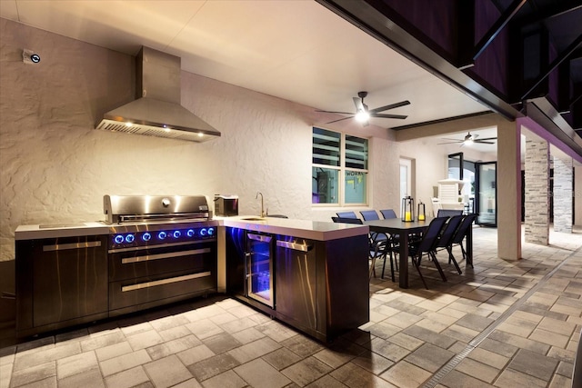 kitchen featuring a textured wall, a peninsula, a sink, wall chimney exhaust hood, and decorative columns