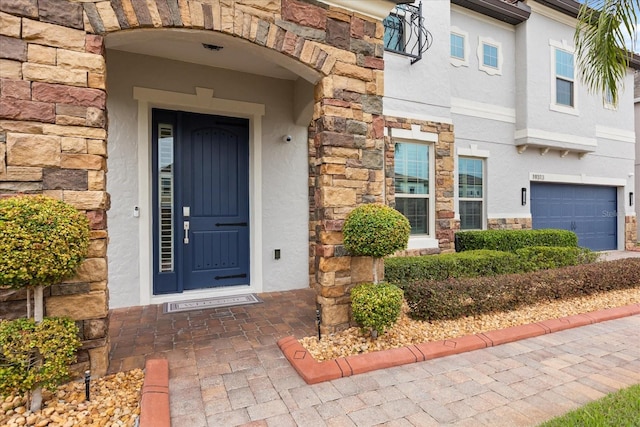 property entrance with an attached garage, stone siding, and stucco siding