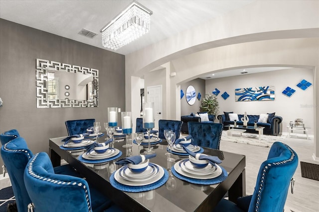 dining area with arched walkways, visible vents, an inviting chandelier, and wood finished floors