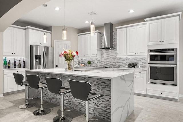 kitchen featuring light stone counters, appliances with stainless steel finishes, white cabinets, a sink, and wall chimney exhaust hood