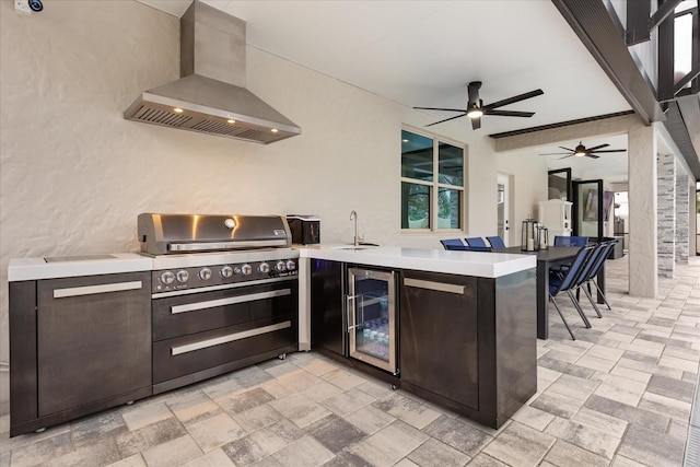 kitchen with light countertops, a sink, beverage cooler, a peninsula, and wall chimney exhaust hood