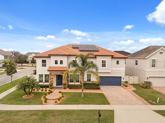 mediterranean / spanish house featuring a garage, a tiled roof, stucco siding, roof mounted solar panels, and a front yard