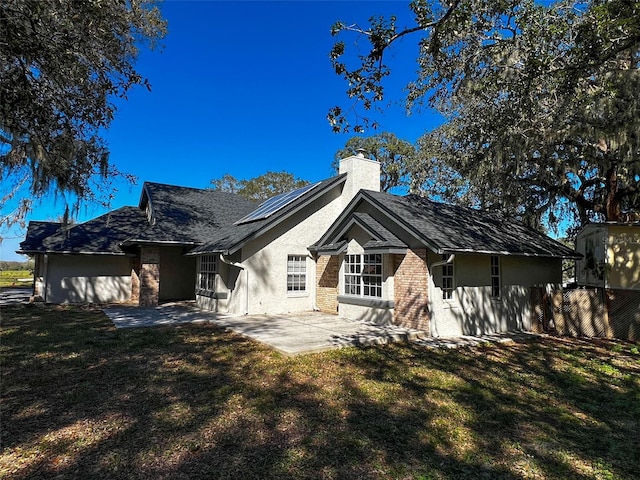 rear view of property featuring a chimney, a patio, a lawn, and solar panels