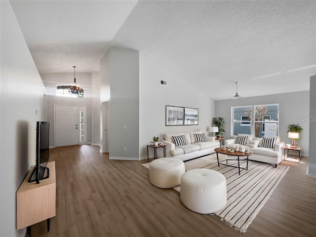 living room with a chandelier, high vaulted ceiling, a textured ceiling, wood finished floors, and visible vents