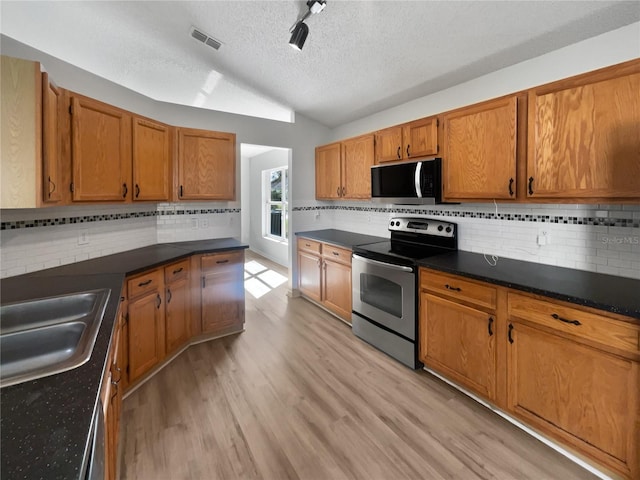 kitchen featuring appliances with stainless steel finishes, dark countertops, brown cabinets, and vaulted ceiling