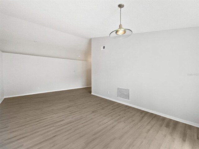 unfurnished room featuring visible vents, vaulted ceiling, baseboards, and wood finished floors