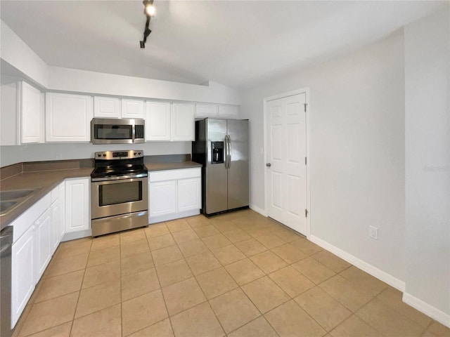 kitchen with stainless steel appliances, dark countertops, white cabinets, vaulted ceiling, and baseboards