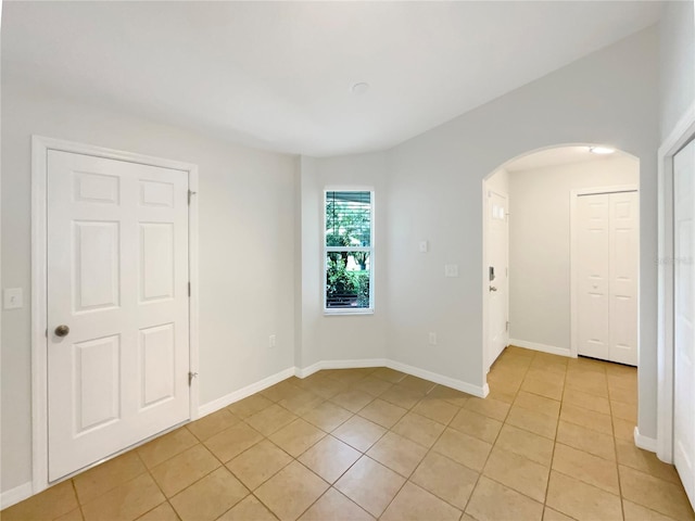 empty room featuring baseboards, arched walkways, and light tile patterned flooring