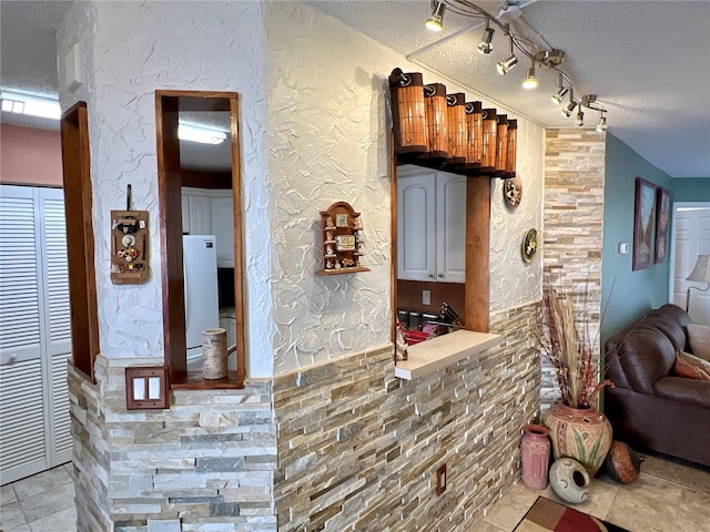 bar with a wainscoted wall, rail lighting, a textured wall, freestanding refrigerator, and a textured ceiling