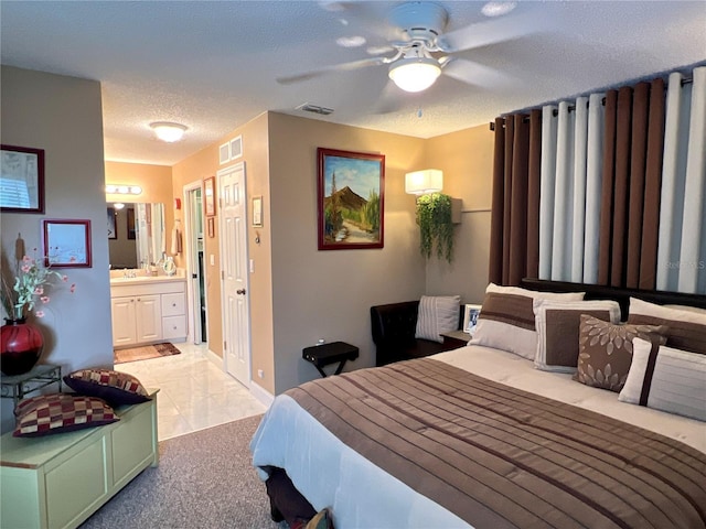 bedroom featuring visible vents, ensuite bathroom, a ceiling fan, light carpet, and a textured ceiling