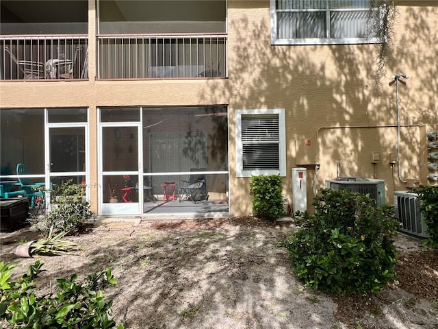 rear view of house with central air condition unit, a balcony, and stucco siding